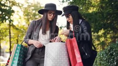 带着购物袋的快乐亚洲女孩正和她站在街上的朋友聊天，然后在街上展示她的购物品